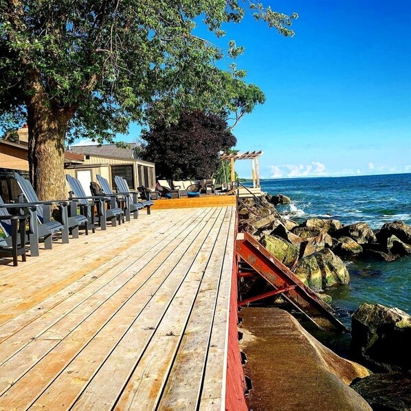 A wooden deck with lounge chairs, a pergola, and a view of the ocean.
