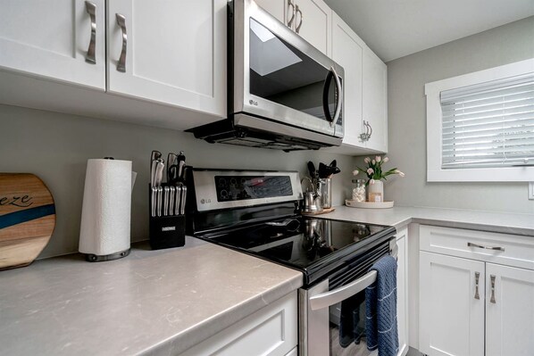 A kitchen with white cabinets, an LG microwave, a stove, and a window with blinds.