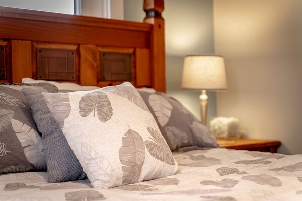 A bed with leaf-patterned pillows, a wooden headboard, and a bedside lamp.