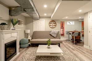 A living room with a fireplace, sofa, coffee table, and a dining area with a bar stool.