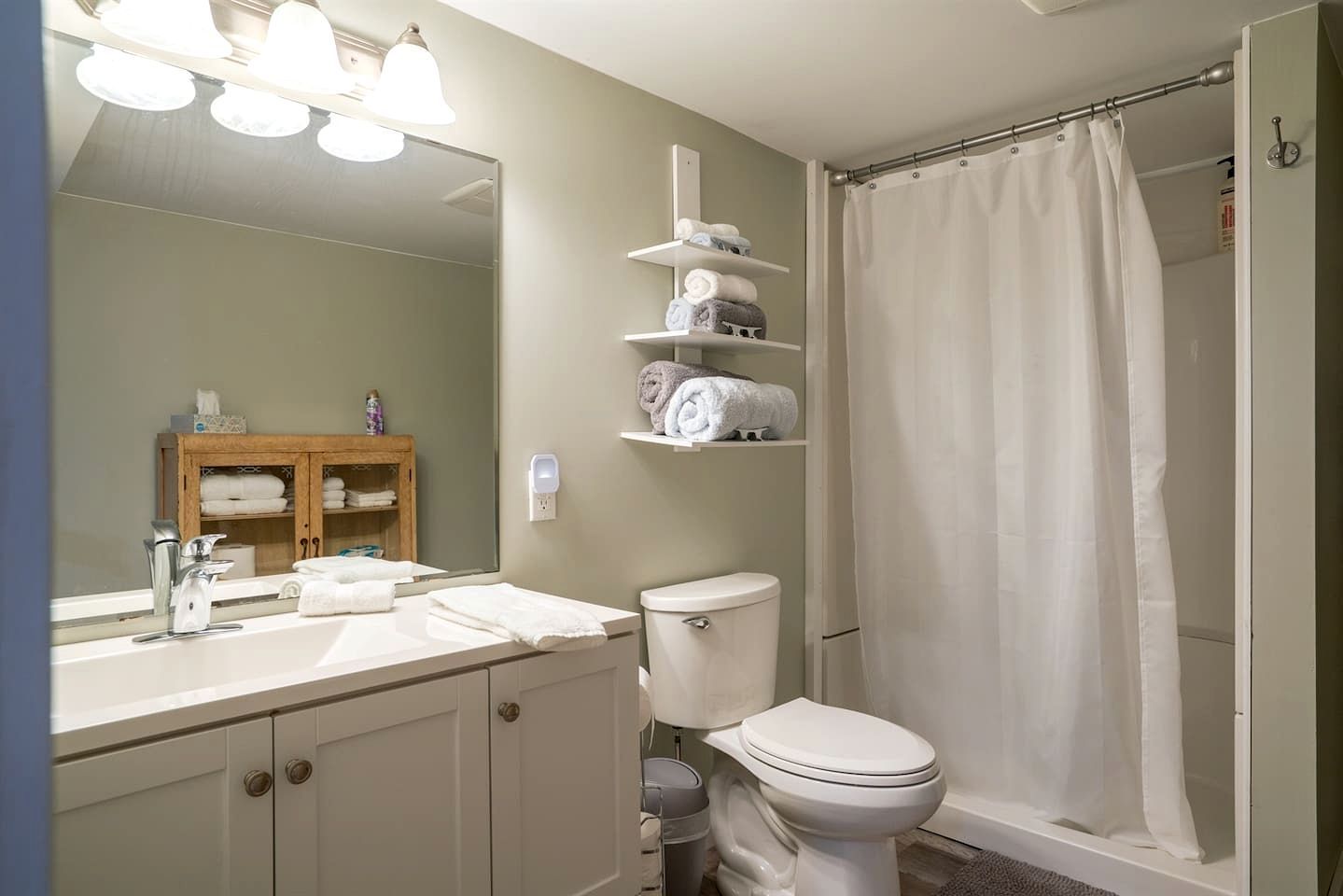 A bathroom with a sink, mirror, toilet, shower curtain, and towel storage.
