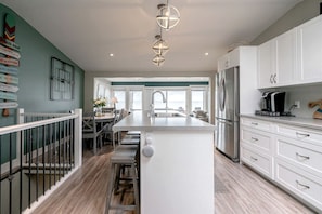 A modern kitchen with white cabinetry, a central island, and a dining area with a view.