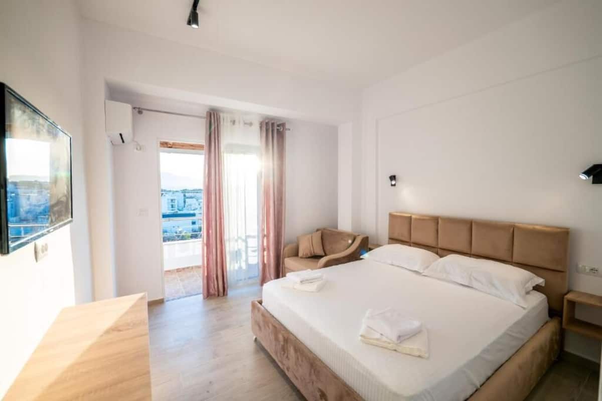Habitación de hotel con cama, una silla, un televisor y vistas a la ciudad.
