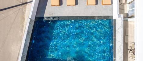 A rectangular swimming pool with clear blue water, surrounded by a concrete deck with lounge chairs.
