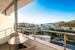 A balcony with a table and chairs, overlooking a coastal town with buildings and hills. - Hotel Perla Ksamil (Ksamil)