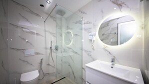 Et moderne badeværelse med brusekabine i glas, et hvidt toilet og en vask med spejl.