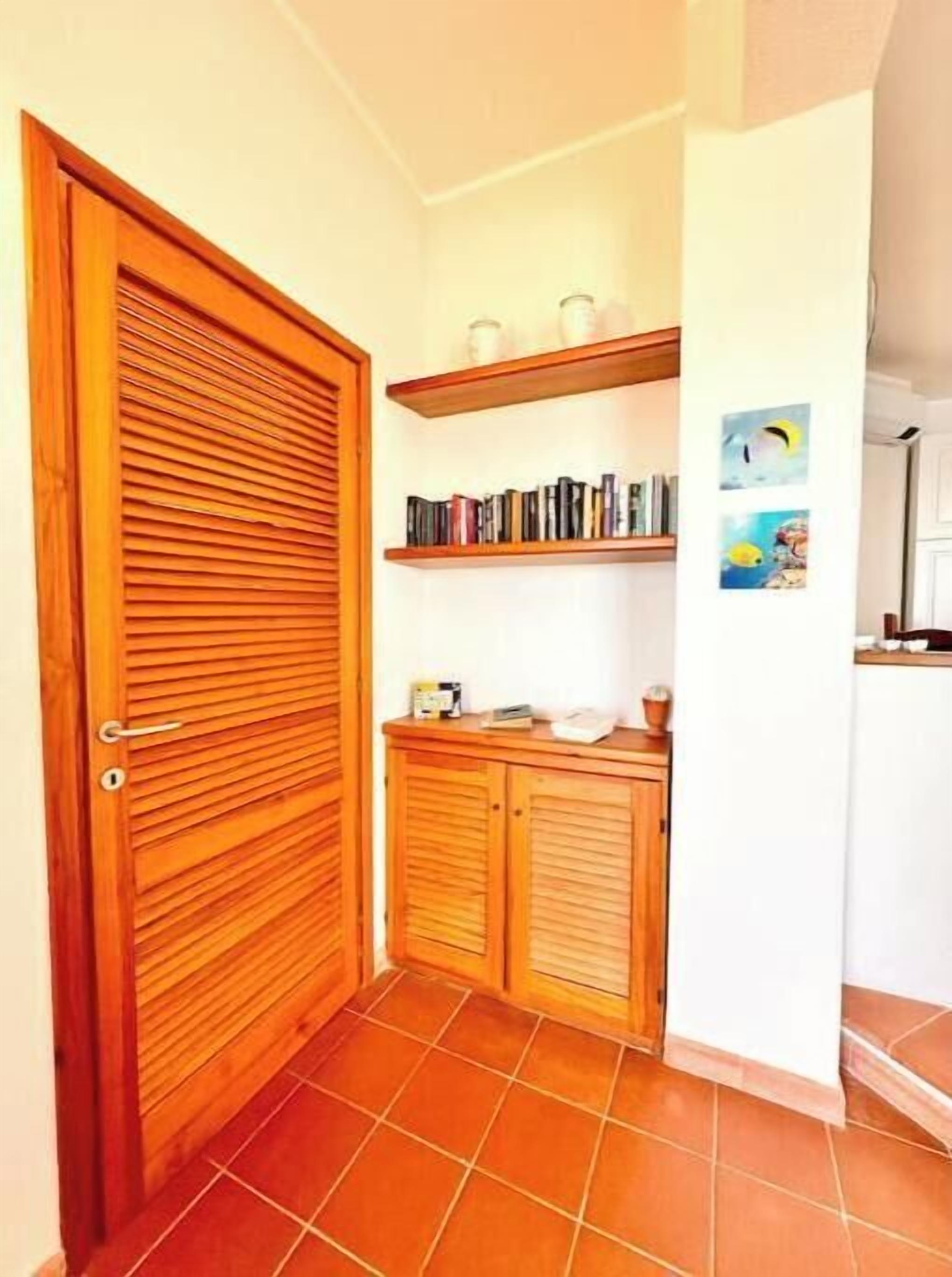 Un couloir avec une porte en bois, un sol carrelé, une bibliothèque remplie de livres et un mur orné d’une affiche.