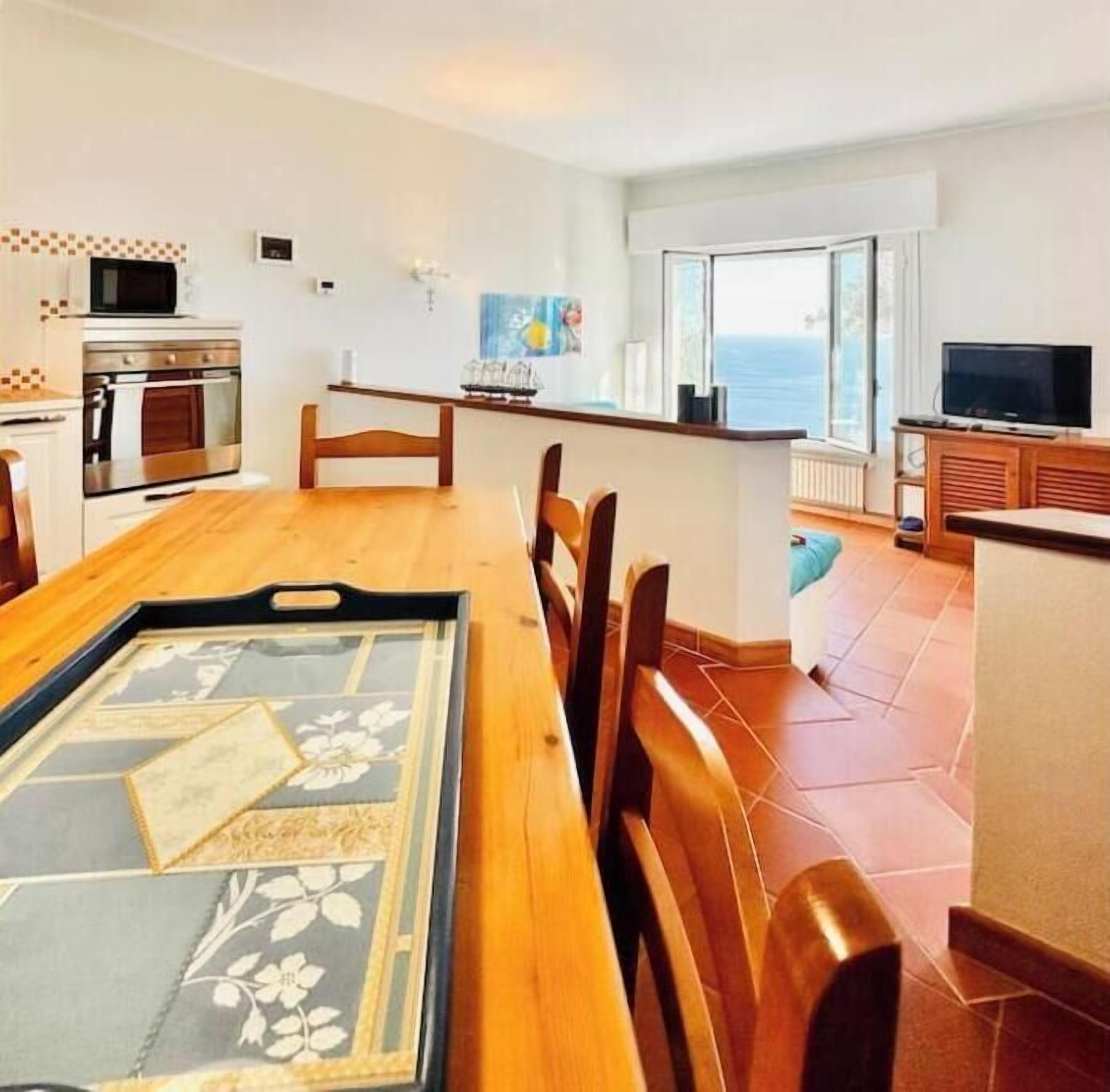 A dining area with a wooden table, chairs, a kitchen with an oven, a microwave, and a TV.