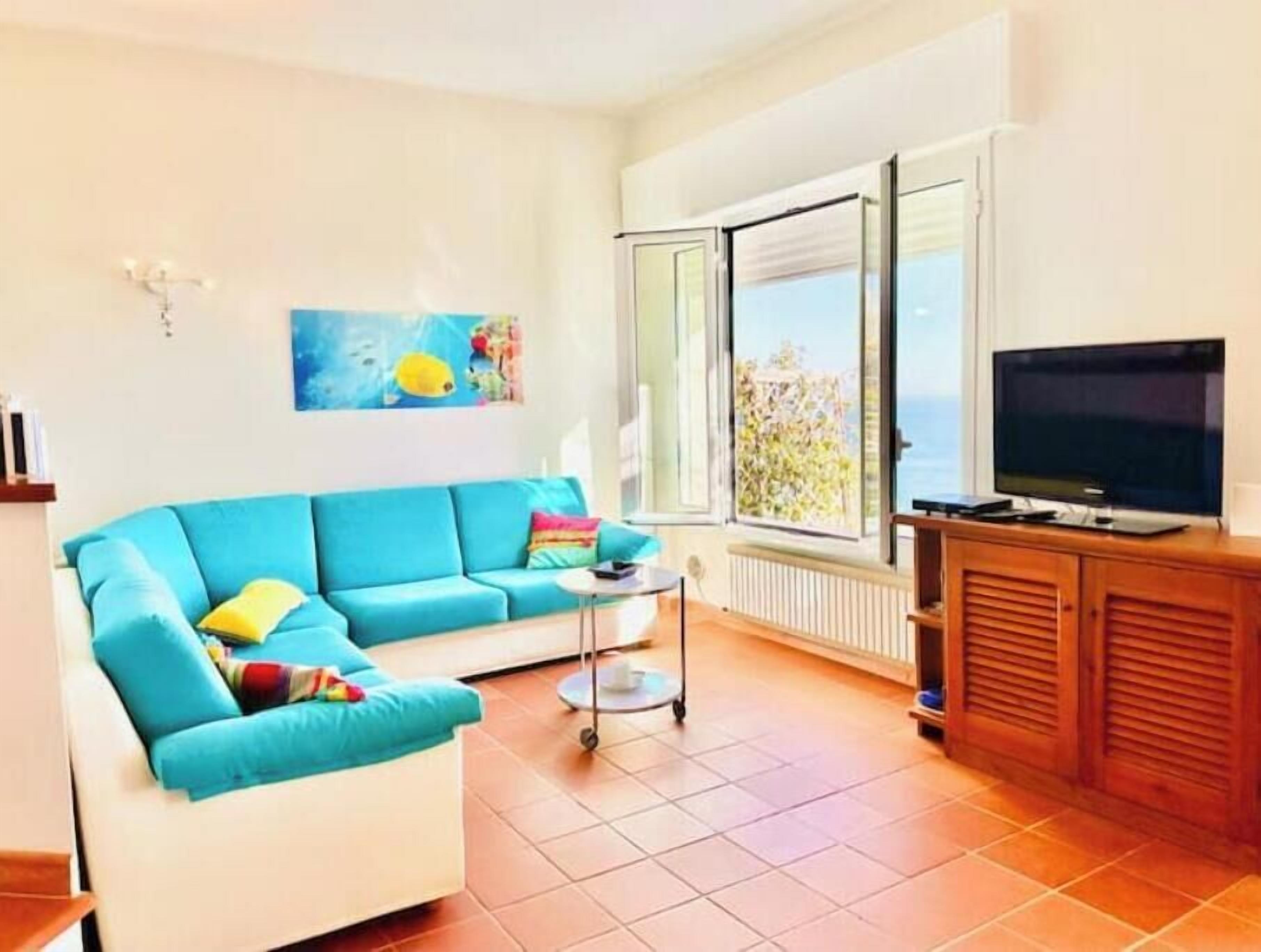 A living room with a blue sofa, a television, a small table, and a window with a view.