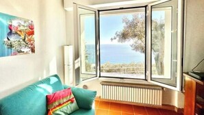 Una stanza con un divano color petrolio, un termosifone e una finestra a bovindo vista mare.