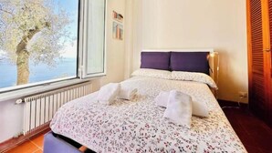 Una camera da letto con un'ampia finestra, un letto con lenzuola bianche, un termosifone e una porta in legno.