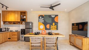 A modern kitchen with wooden cabinets, a built-in oven, a refrigerator, and a dining area with a table and chairs. - Lekatika Villa (Kerobokan)