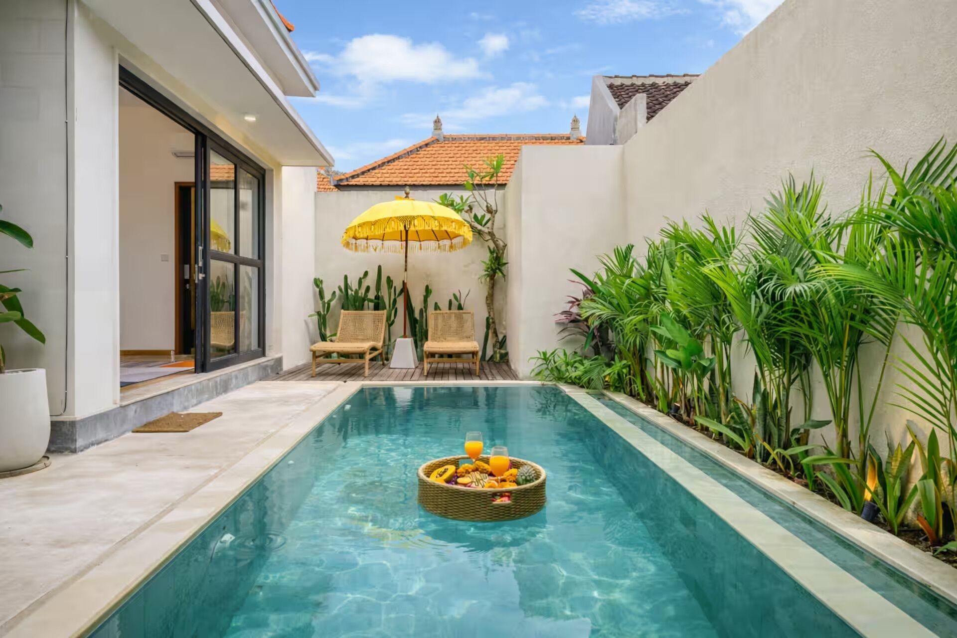 A swimming pool with a wicker basket of fruits and a yellow umbrella.