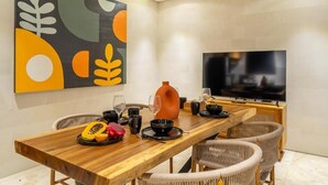 A dining area with a wooden table, wicker chairs, a TV, and a colorful abstract painting on the wall. - Lekatika Villa (Kerobokan)