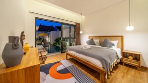 A modern bedroom with a bed, bedside tables, a desk, and a view of an outdoor pool area. - Lekatika Villa (Kerobokan)