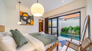 A bedroom with a bed, a chair, a painting, and a view of an outdoor pool. - Lekatika Villa (Kerobokan)