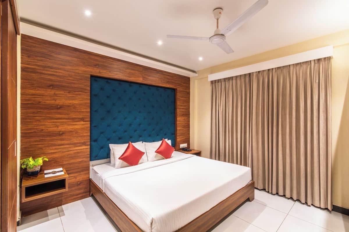 A hotel room with a bed, wooden headboard, a ceiling fan, a bedside table, and a window with curtains.