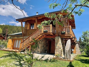 Ein Holzhaus mit Steinuntergrund, einer Holztreppe und einem Balkon mit Blumentöpfen.