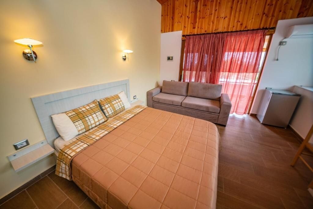 A bedroom with a bed, a sofa, a lamp, and a window with curtains.