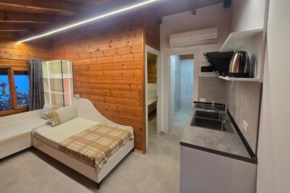 A compact room with a bed, a small kitchenette, and a wooden wall.