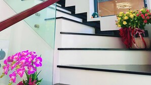 Una escalera moderna con barandillas de vidrio y barandilla de madera, que lleva a un rellano con un ventanal grande y un equipo de aire acondicionado instalado en la pared.