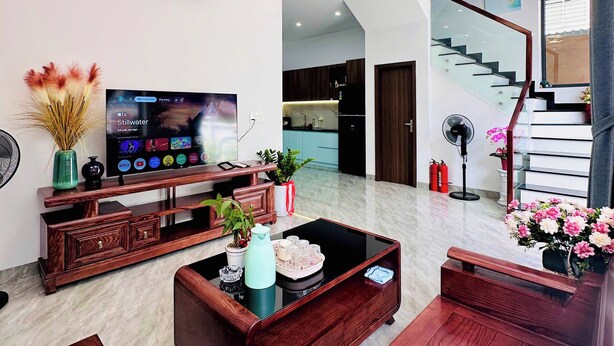 Una sala de estar moderna con un televisor de pantalla plana, muebles de madera, una escalera y una lámpara en el techo.