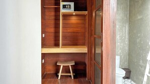 Un baño pequeño y compacto con paredes de madera, un taburete de madera, un inodoro y un estante con un pequeño electrodoméstico.