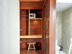 Ein kleines, kompaktes Badezimmer mit Holzwänden, einem hölzernen Hocker, einer Toilette und einem Regal mit einem kleinen Gerät.