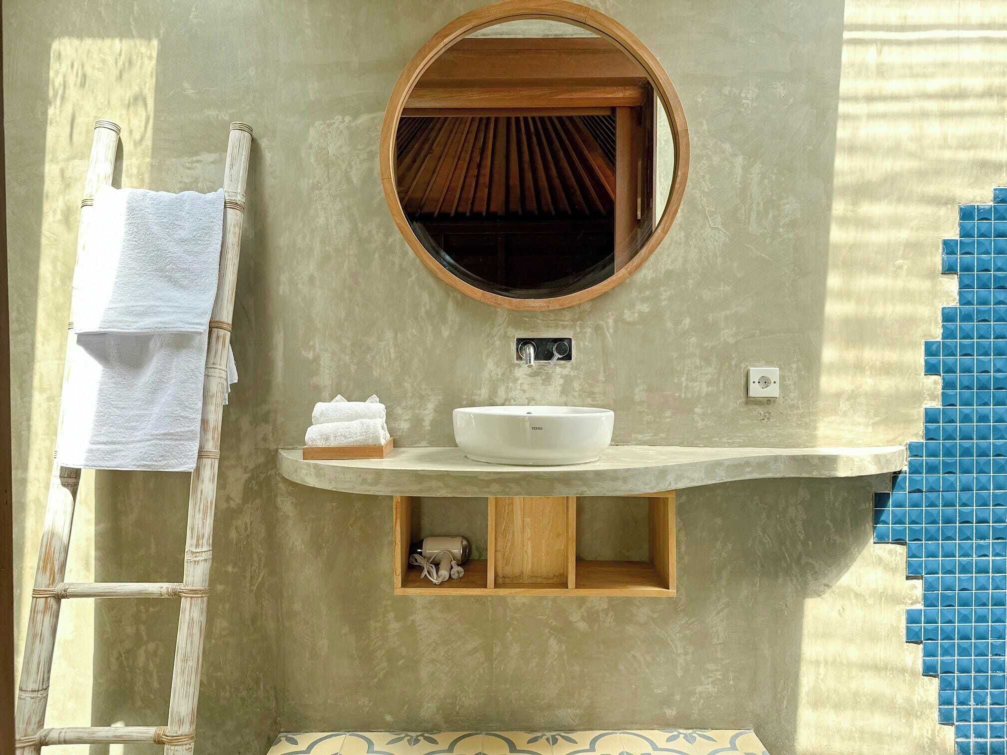 A bathroom with a round mirror, a sink, a towel rack, and a shelf with toiletries.