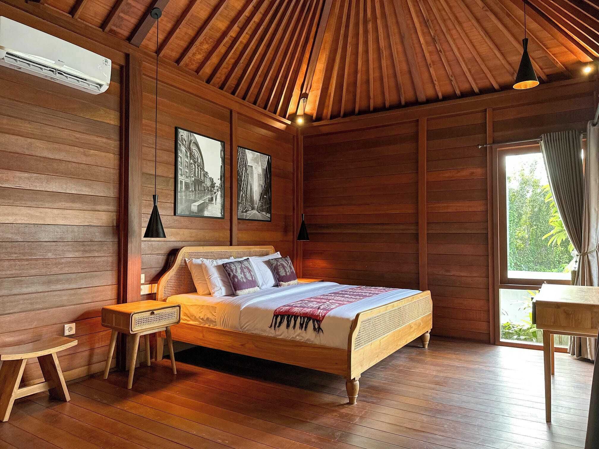 Una habitación con paneles de madera, una cama, una mesita de noche, una mesa y un ventanal con cortinas.