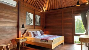 Una habitación con paneles de madera, una cama, una mesita de noche, una mesa y un ventanal con cortinas.