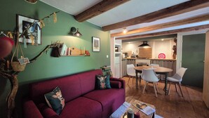 Una sala de estar acogedora con un sofá rojo, una mesa de comedor con sillas, una cocina al fondo y un techo de madera.