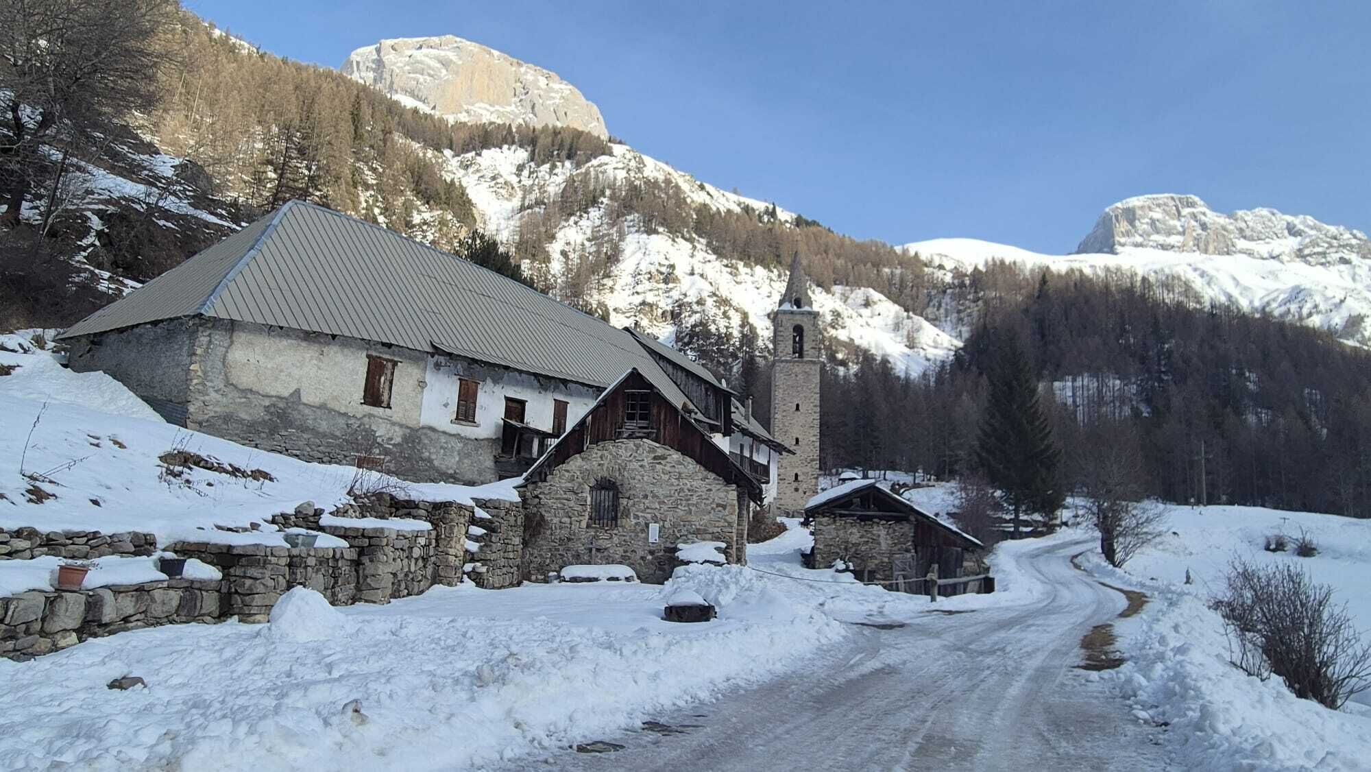Un bâtiment en pierre doté d’un clocher, entouré de montagnes enneigées.