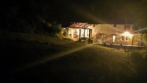 Una cabaña rústica con fachada de madera, puerta de cristal y un interior visible con comedor.
