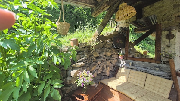 A rustic stone wall, wooden bench, hanging baskets, and a potted plant in a garden setting. - Studio Le Mélèze (Méolans-Revel)