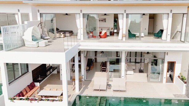 Un moderno edificio residencial de varios niveles con piscina interior de vidrio, zonas de estar al aire libre y una combinación de espacios de vida interiores y exteriores.