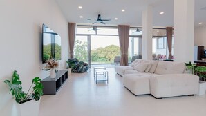 Una sala de estar moderna con un sofá blanco, un televisor de pantalla plana y ventanas grandes.