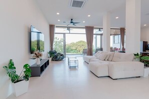 Ein modernes Wohnzimmer mit einem weißen Sofa, einem Flachbildfernseher und großen Fenstern.