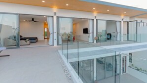 Un interior moderno con barandilla de vidrio, una zona de estar con sofás y un televisor de pantalla plana montado en la pared.