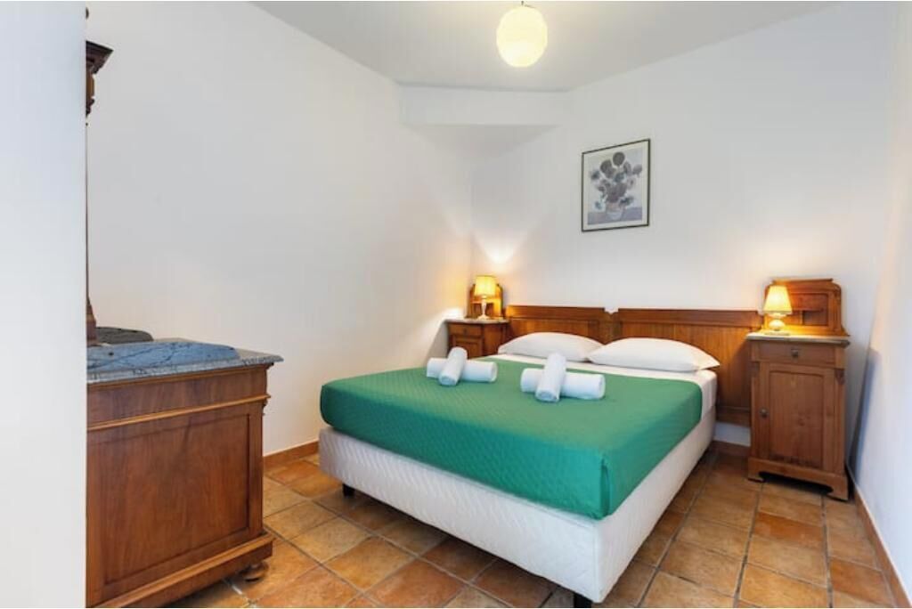 A single bed with a green bedspread, two bedside lamps, a wooden headboard, a nightstand, and a small cabinet.