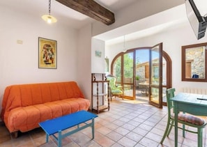 Sala de estar com sofá, mesa e um banco. Há uma porta que dá para uma varanda.