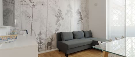 Un salón moderno con un sofá gris, una mesa de comedor de vidrio y una pared con un mural de un árbol y ciervos.