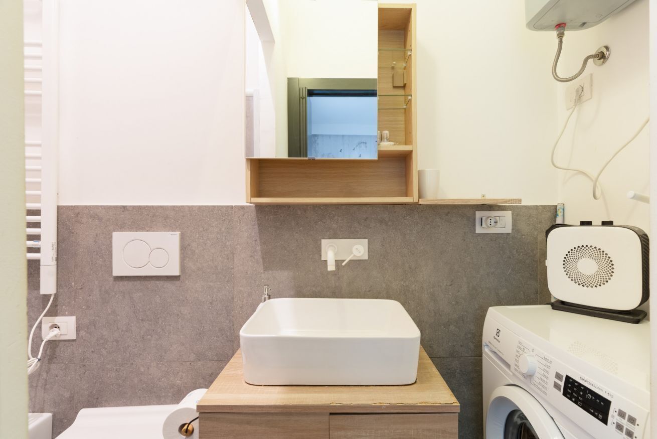 A bathroom with a white sink, a mirror, a wooden vanity, a washing machine, and a towel rack.