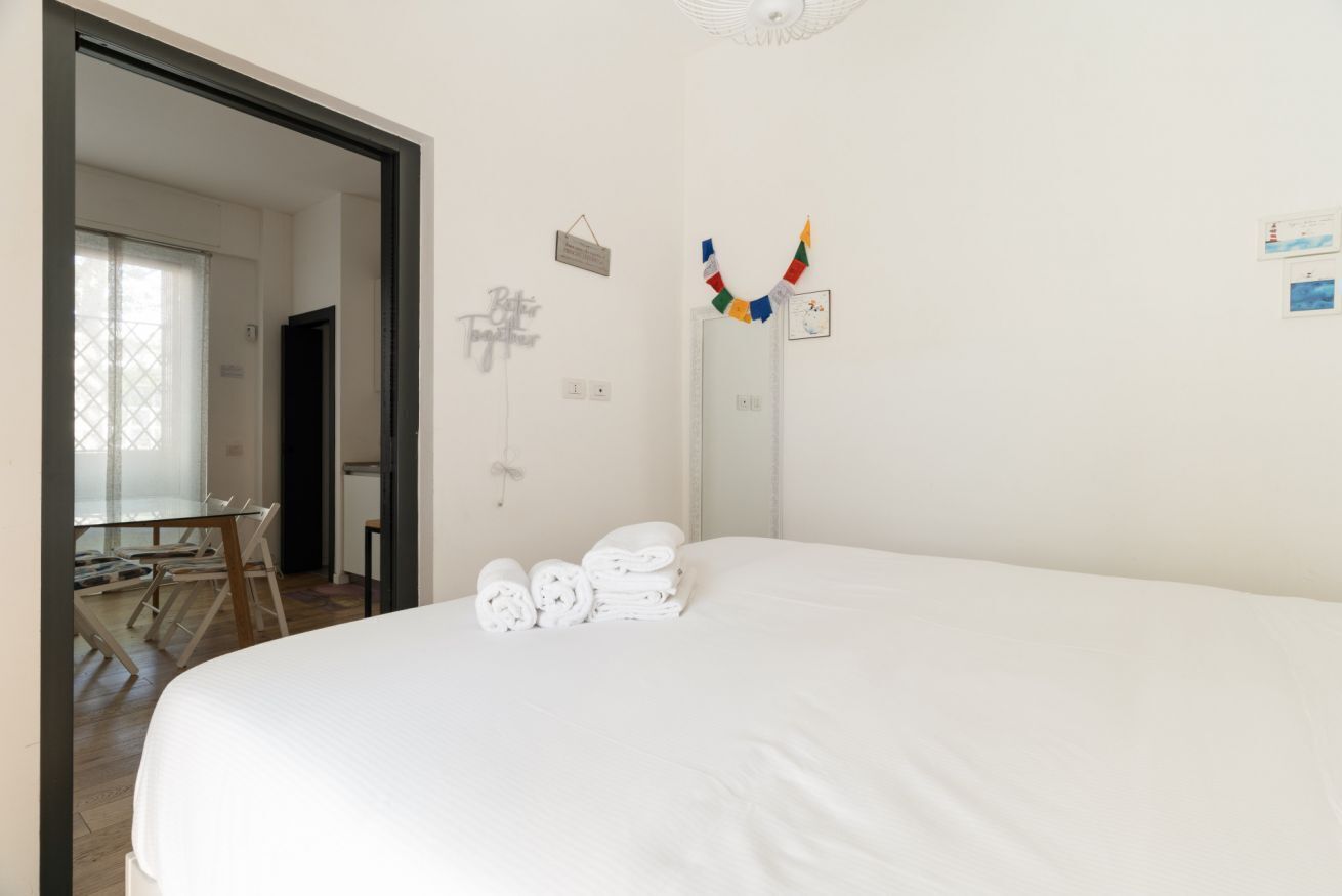Een slaapkamer met een bed, een bureau en een stoel. Er liggen handdoeken op het bed.