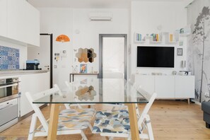 Een moderne keuken met een glazen eettafel, witte kasten en een flatscreen televisie.