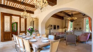 A dining area with a wooden table set for six, surrounded by chairs. There is a chandelier above the table, and a sofa with cushions in the background. - Domaine de la Rose Comtesse - Luxe (Ventabren)