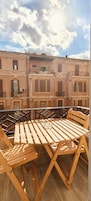 Una mesa y sillas de madera en un balcón con vistas a un edificio rosado con balcones.