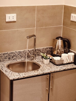 Una cocina con un lavamanos de acero inoxidable, una cafetera y una bandeja con tazas y una planta.