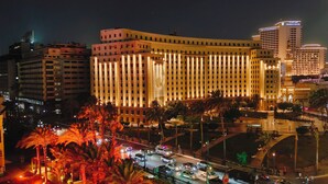 Um hotel com fachada vertical marcante, vários andares e entrada bem iluminada.