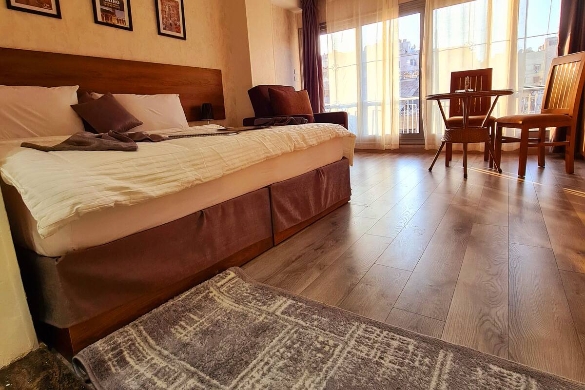 A hotel room with a large bed, a sitting area with a table and chairs, and a balcony with curtains.